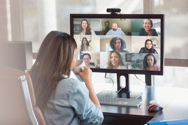A woman at a desk looks at a computer screen showing a virtual meeting